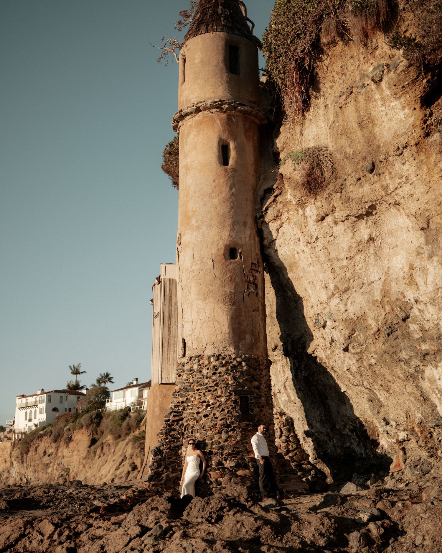 A historic lighthouse tower stands against a rocky cliff by the ocean.