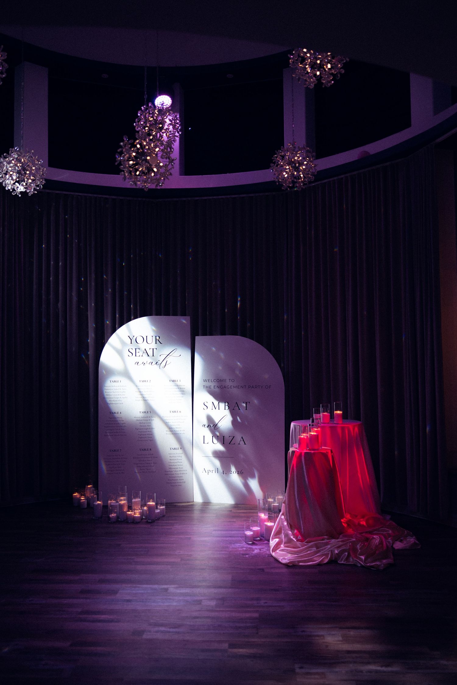 Wedding seating chart display with dramatic purple lighting and red draped table decor.