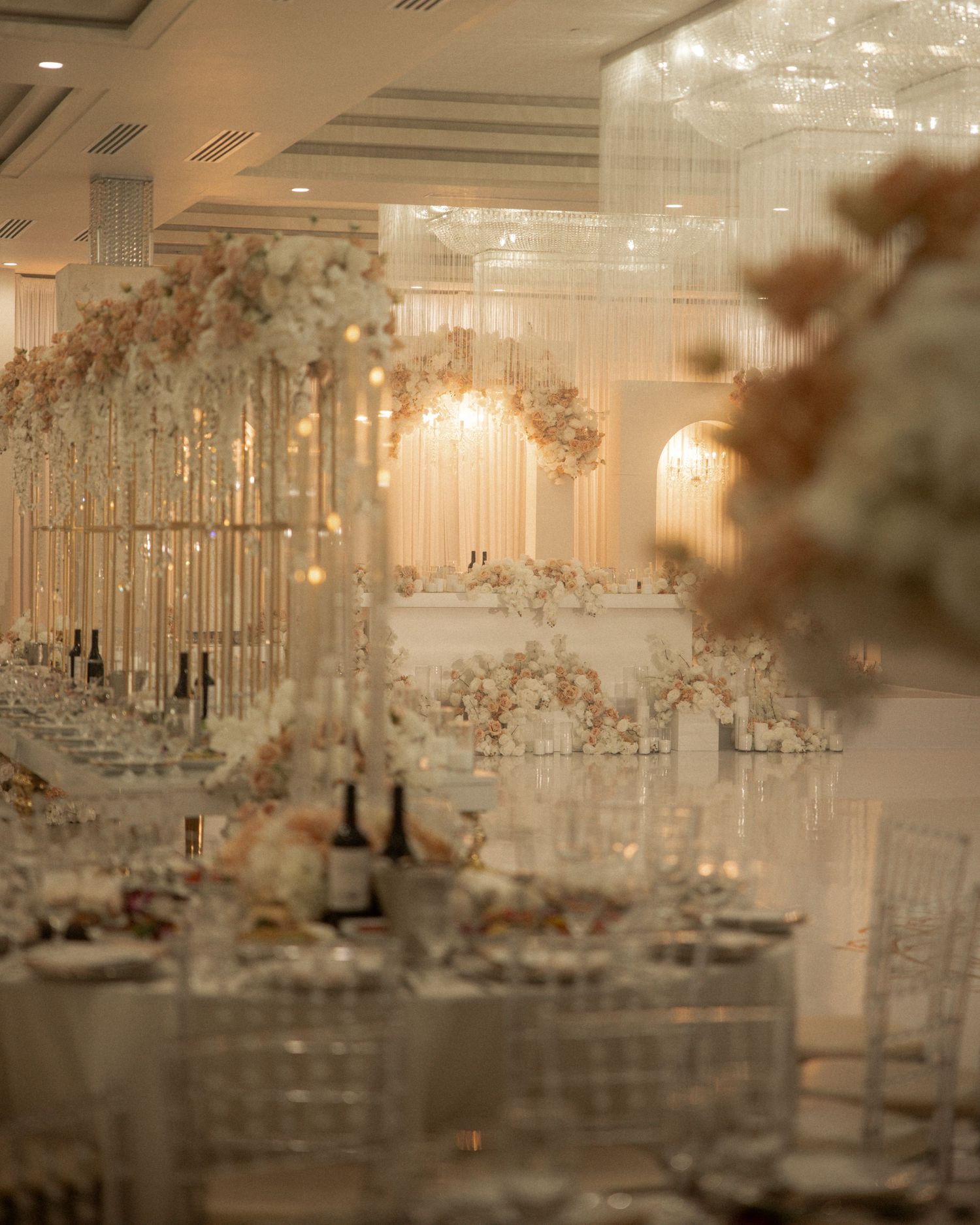 Luxurious wedding reception hall with crystal chandeliers, white floral centerpieces, and elegant table settings.