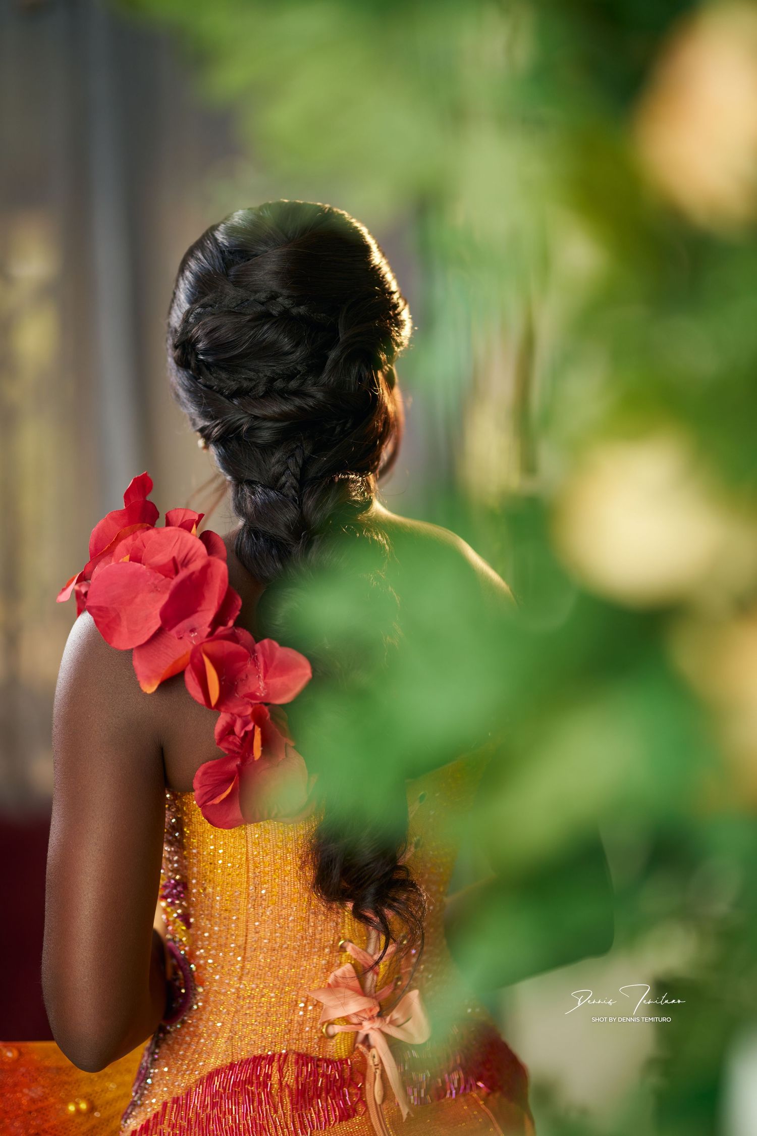 Back view of a person wearing a yellow dress with red flowers against a blurred natural background.