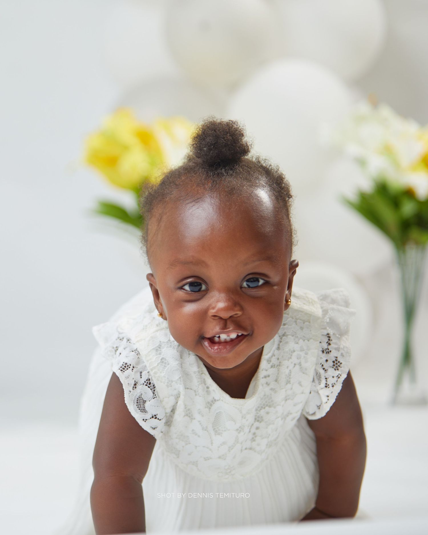 Sweet expressions in white lace dress against light background with yellow flowers.