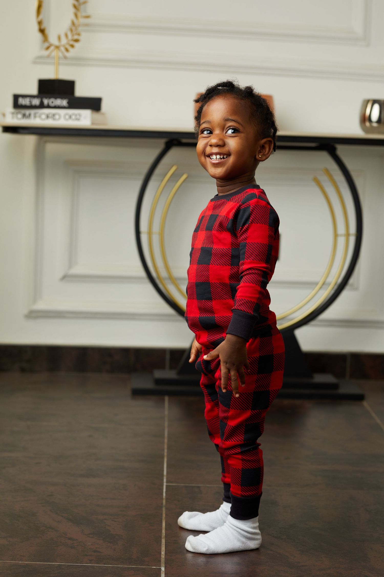 Playful poses in red buffalo plaid outfit on dark hardwood floor.