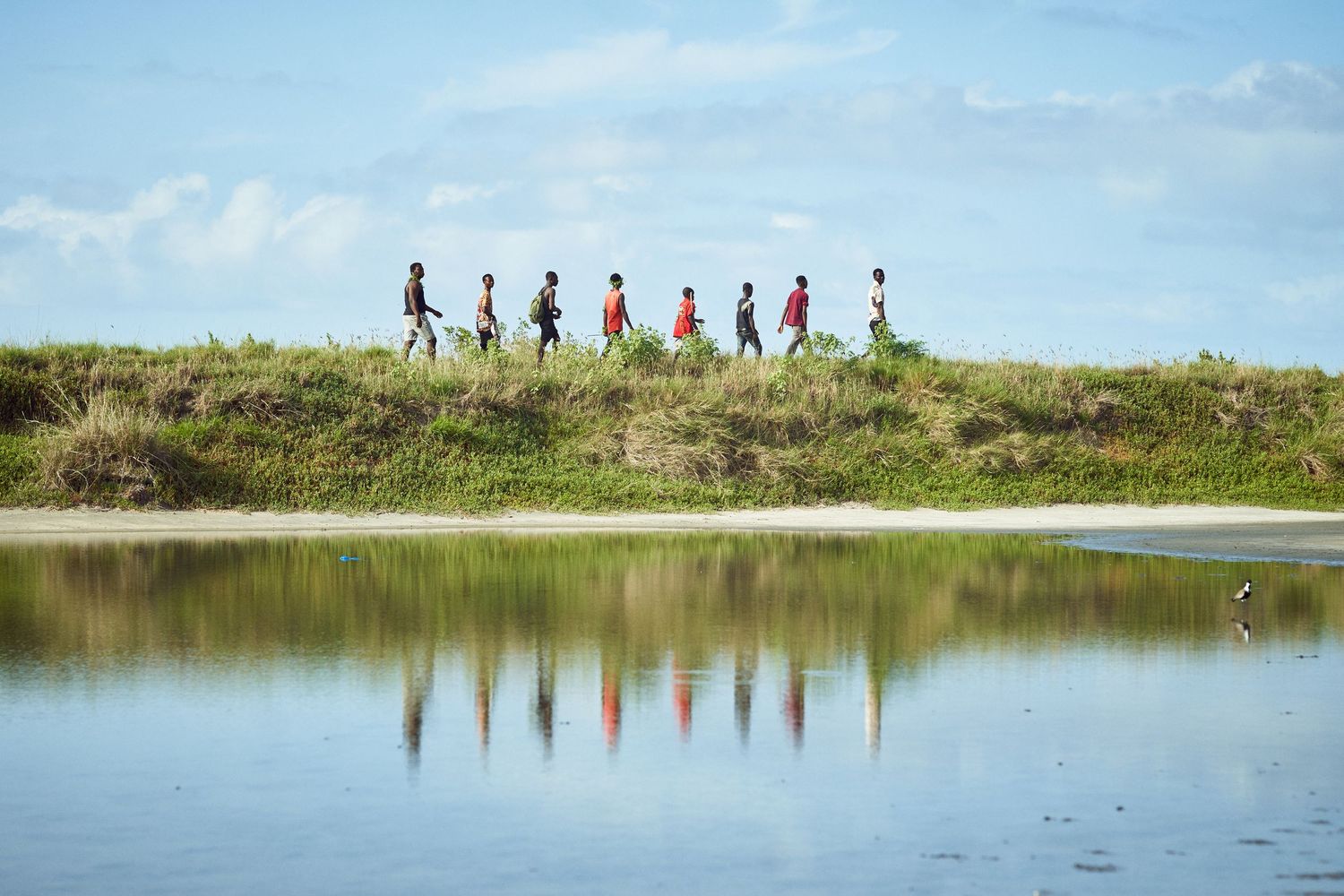 Silhouettes of people walking along a hilltop reflected in calm water below.