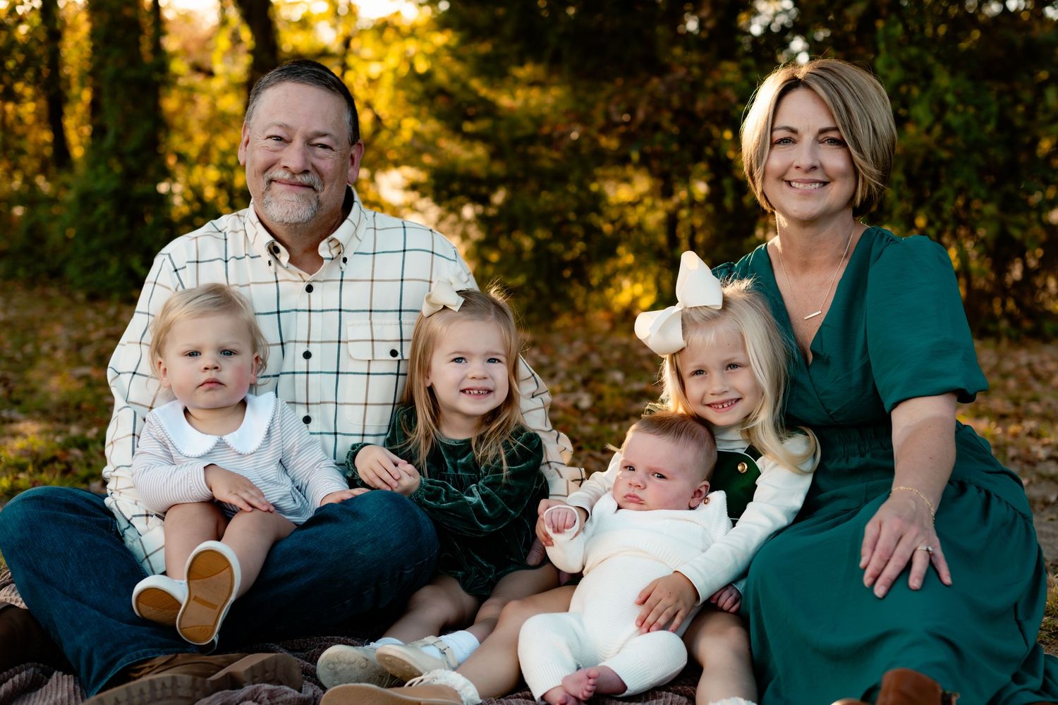 A family sits together outdoors during golden hour sunset in coordinating white, green and navy outfits.
