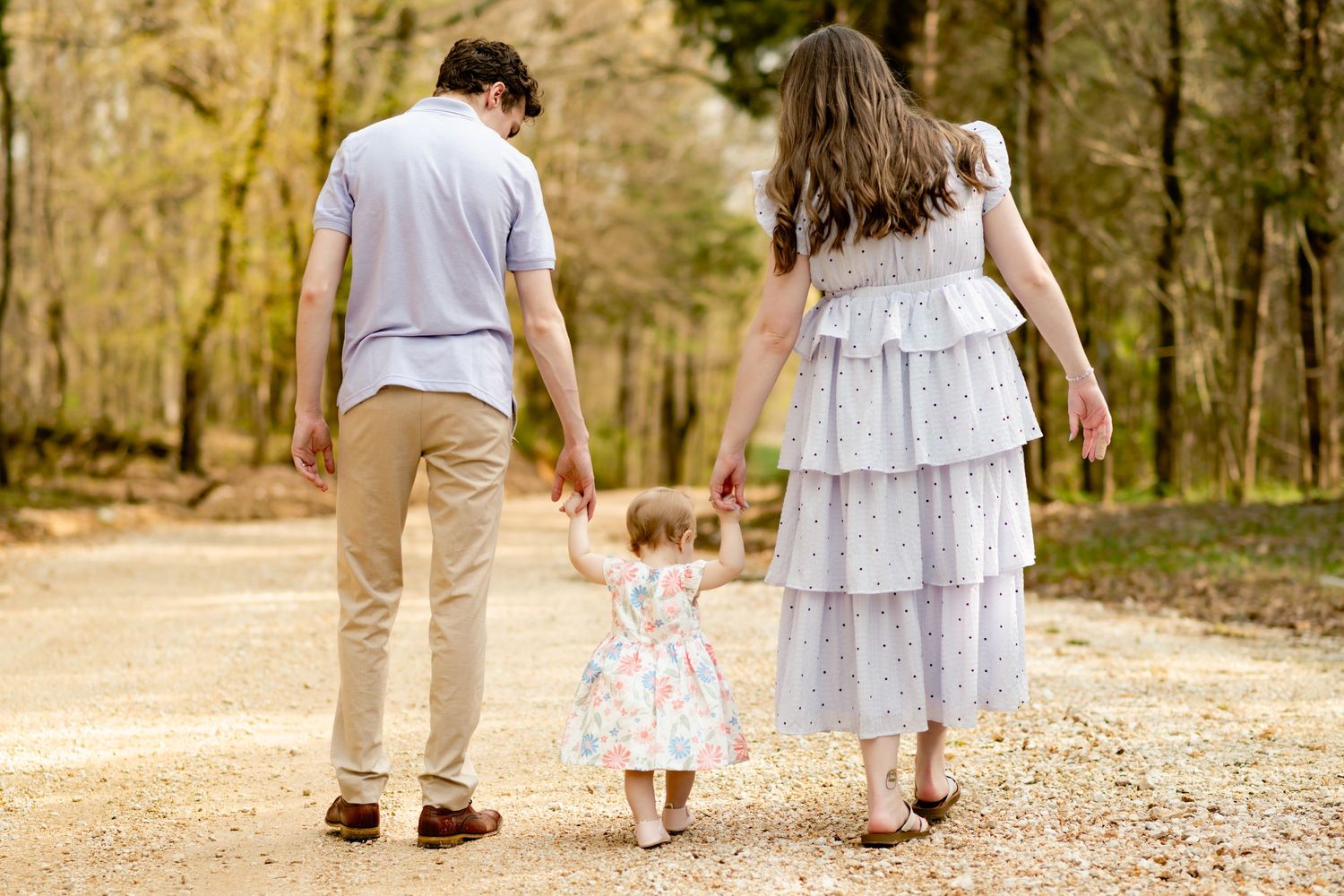 Family walking down wooded path together holding hands.