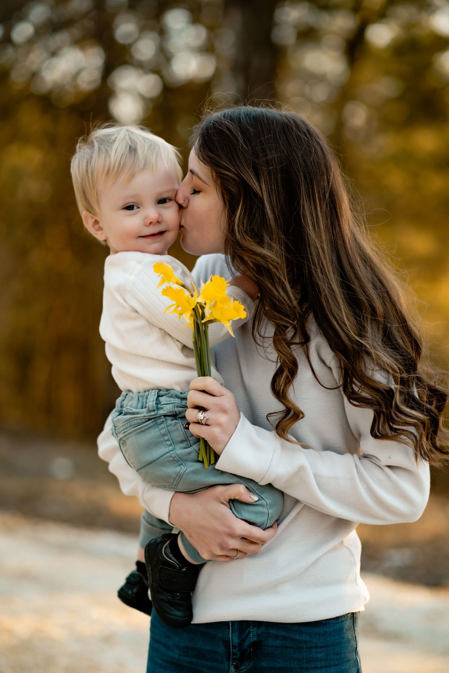 Tender moment with parent and child holding yellow daffodils against autumnal background.