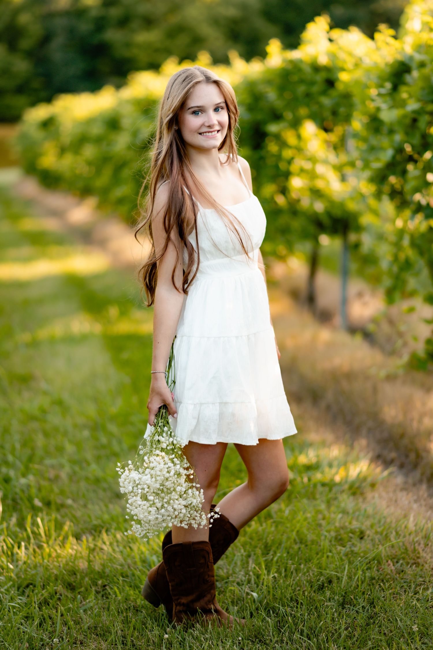 Summer portrait in white dress and brown boots among vineyard rows.
