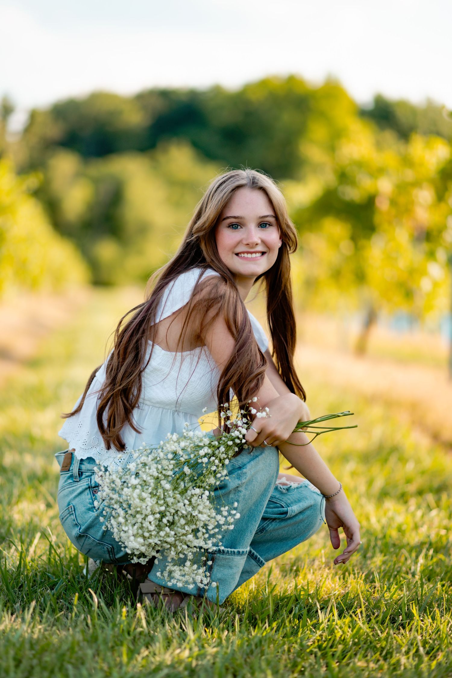 Portrait with wildflowers in white top and jeans during golden hour photoshoot.