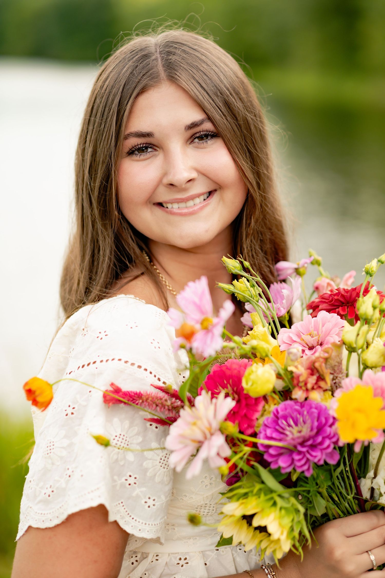 Portrait holding colorful bouquet of summer flowers in white eyelet dress outdoors.