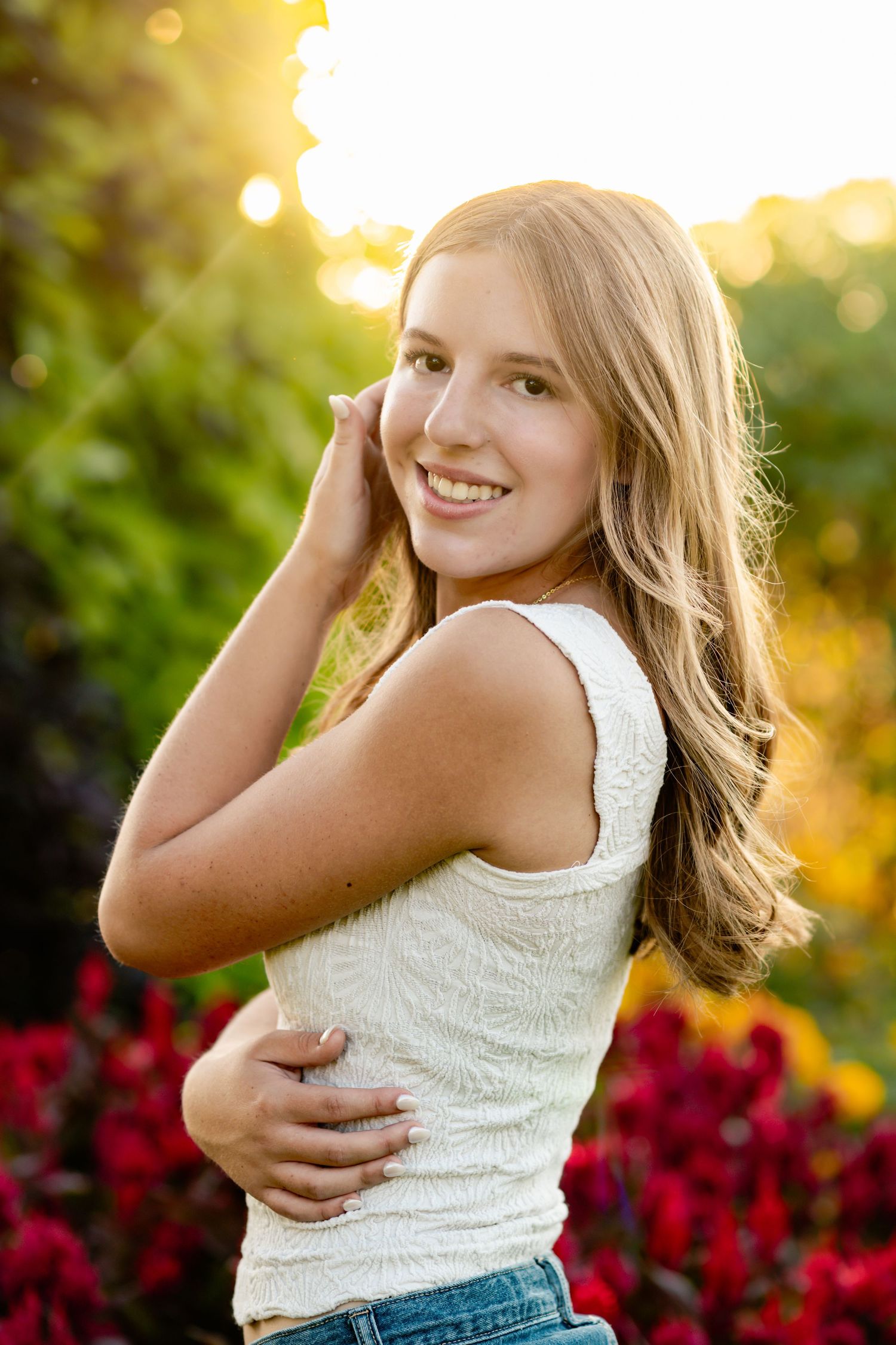 A series of golden hour portraits showing someone in a white lace top and jeans against vibrant red flowers at sunset.
