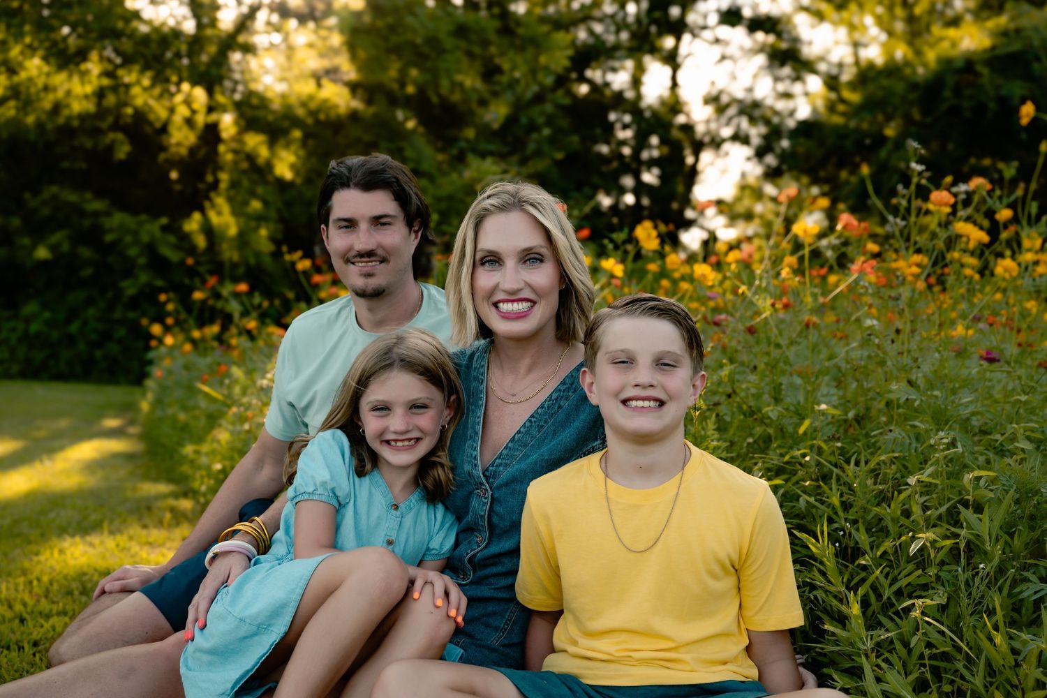Family group smiles together in blooming meadow with their white dog.
