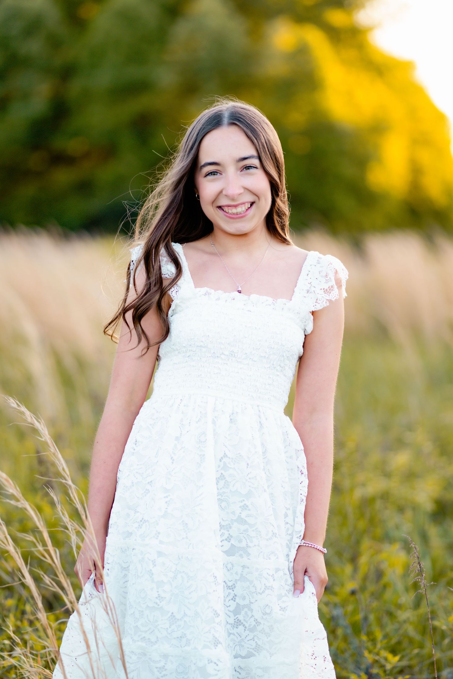 A white lace dress stands out against tall grass and golden sunlight in an outdoor portrait setting.