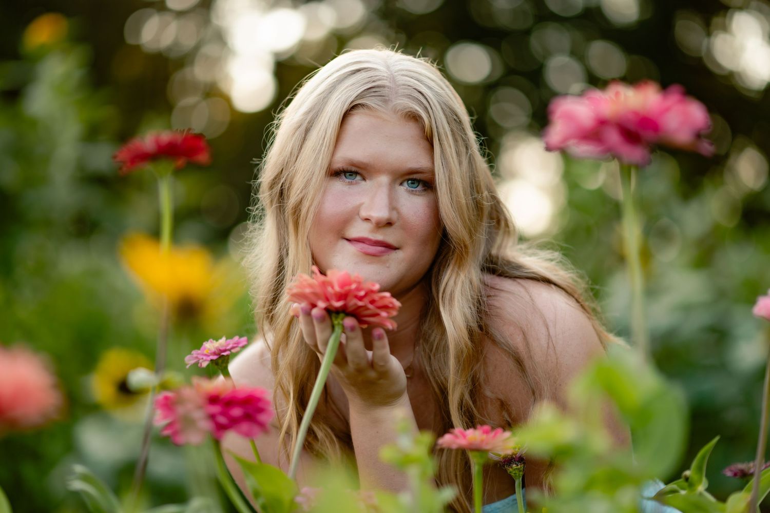 A cheerful person poses among colorful zinnia flowers in a summer garden with soft bokeh background.