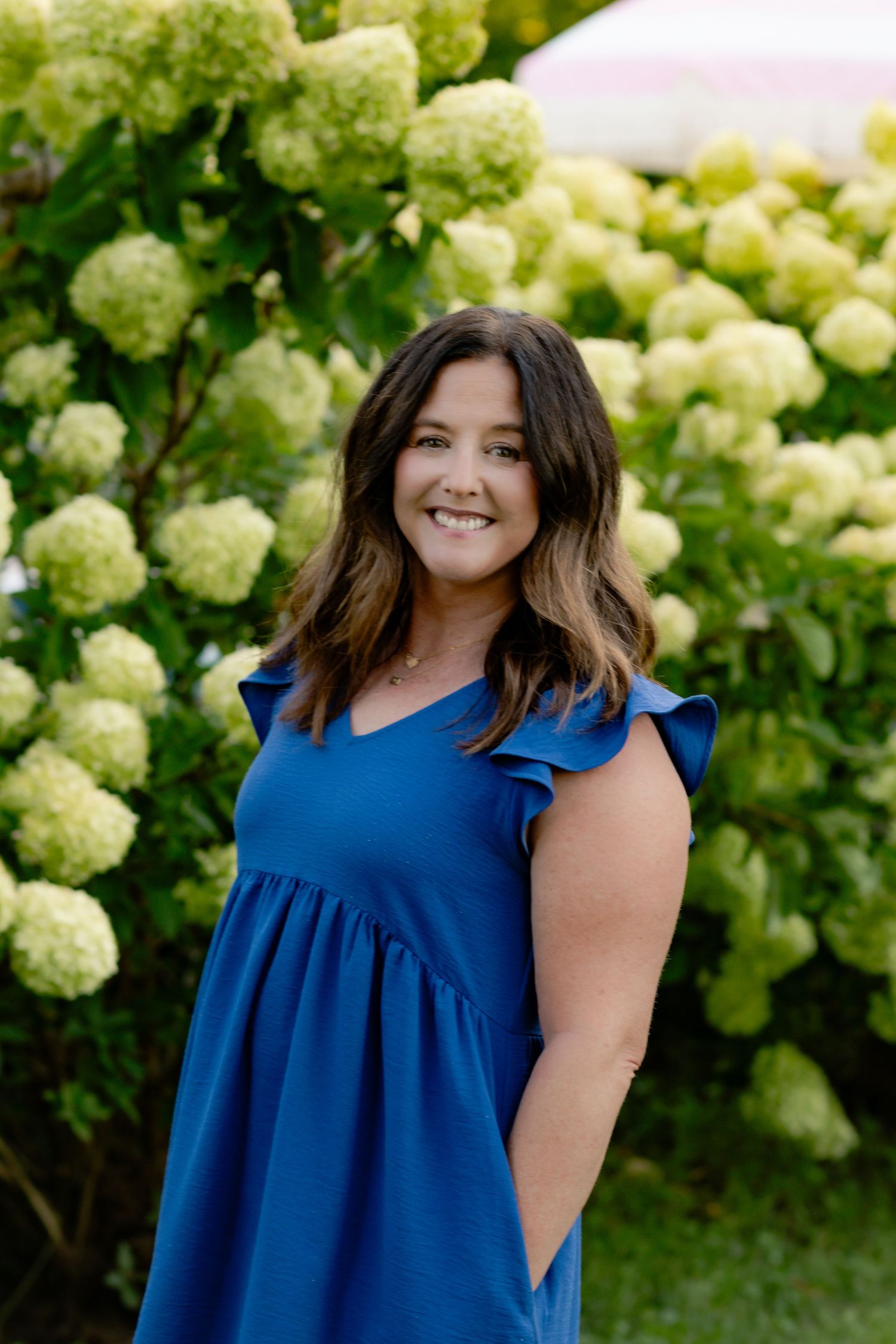 A series of portrait photos in front of blooming hydrangea bushes featuring someone wearing a blue ruffle dress.