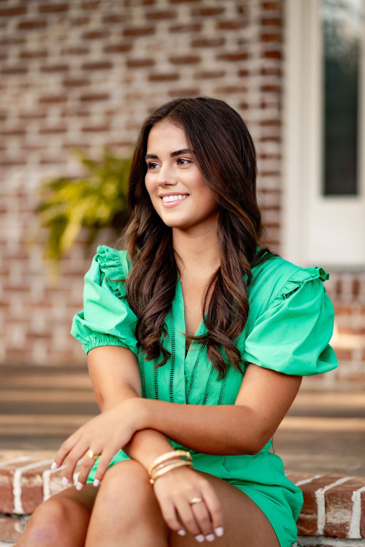 A portrait series in a bright green dress sitting on brick steps during a summer photoshoot.