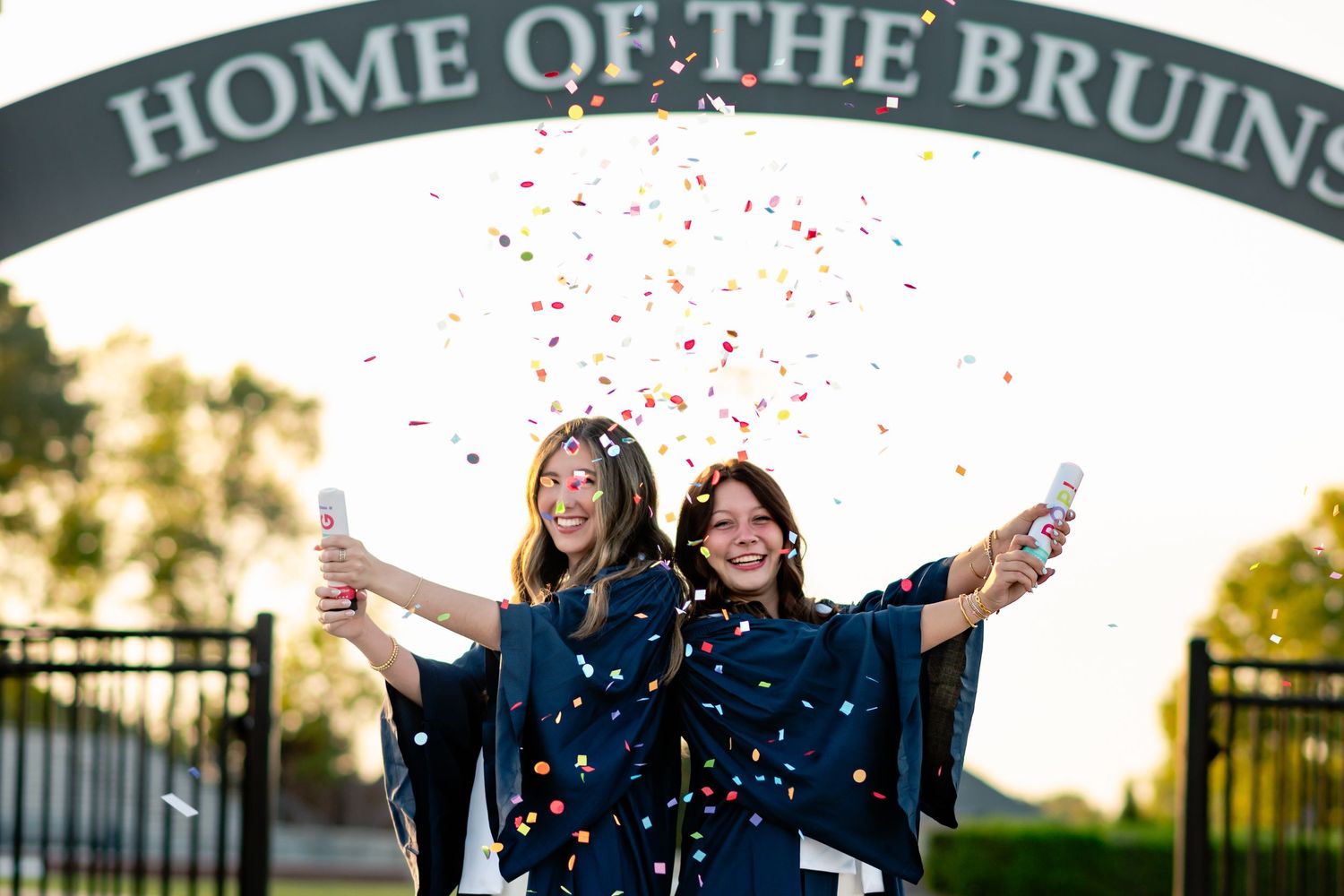 Confetti falls as graduates celebrate under Home of the Bruins sign.