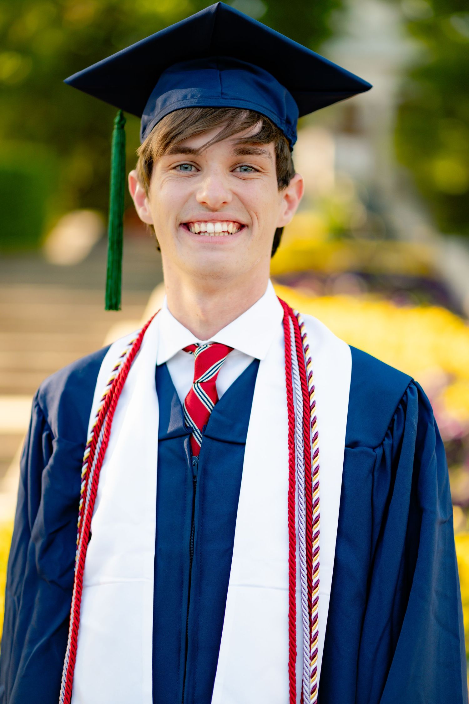 Graduate in blue academic regalia smiles while wearing decorated stoles.