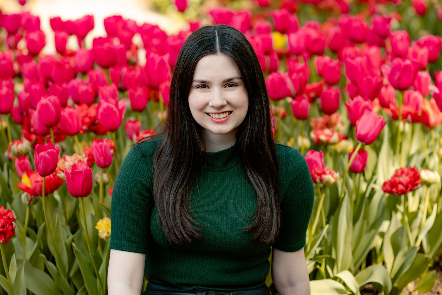 A person in a dark green top poses among vibrant red tulip flowers in a spring garden setting.