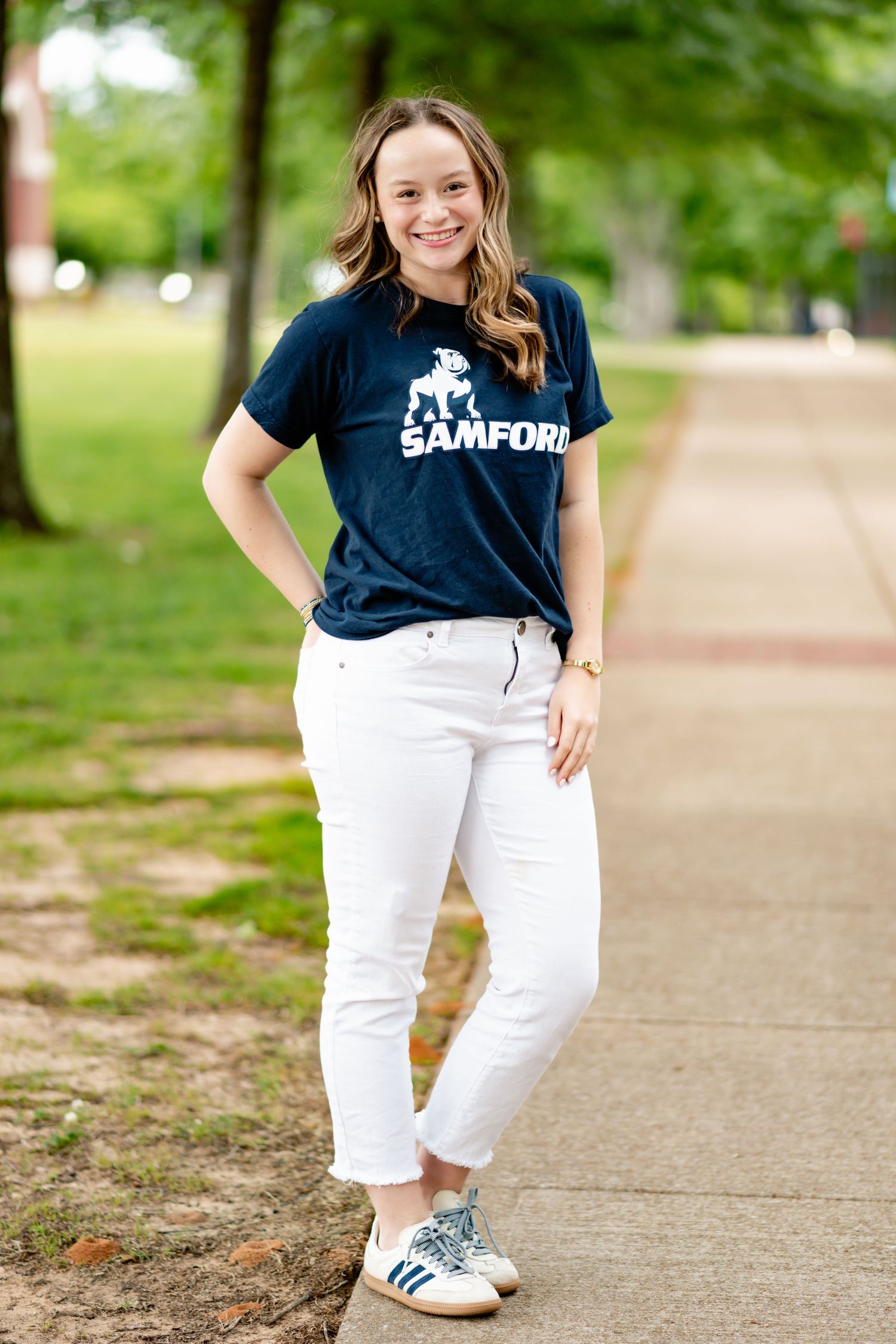 Student in Samford shirt and white pants poses on campus walkway.