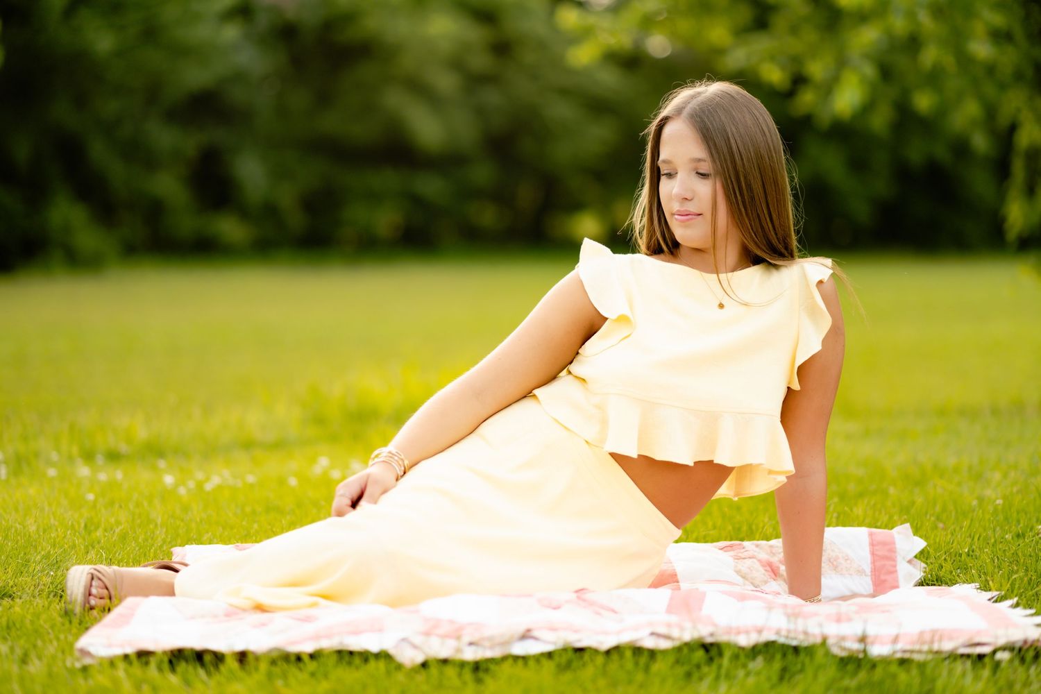Someone in a peach dress lies on a blanket in a sunny green field during an outdoor photo session.