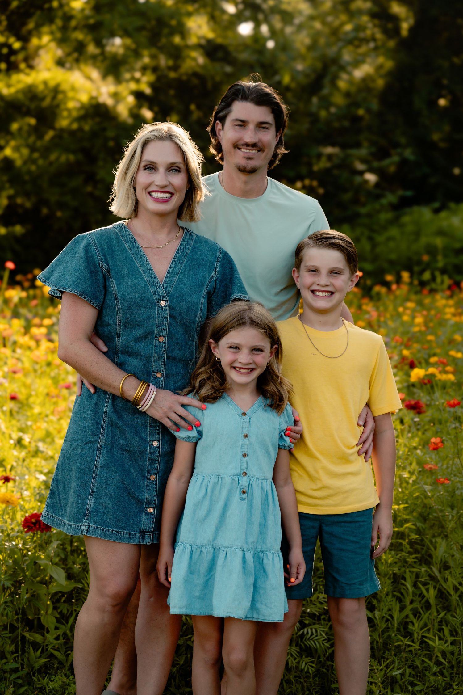 Happy family of four posing together in field of yellow wildflowers at sunset.