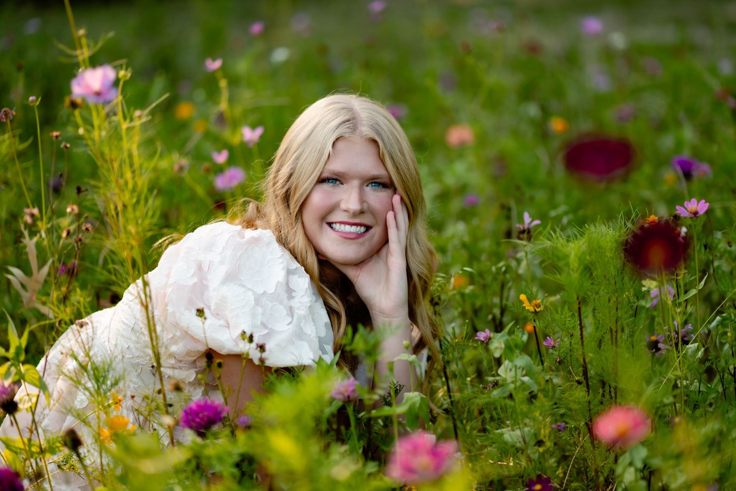A person lies in a vibrant wildflower meadow with pink and white blooms on a sunny summer day.