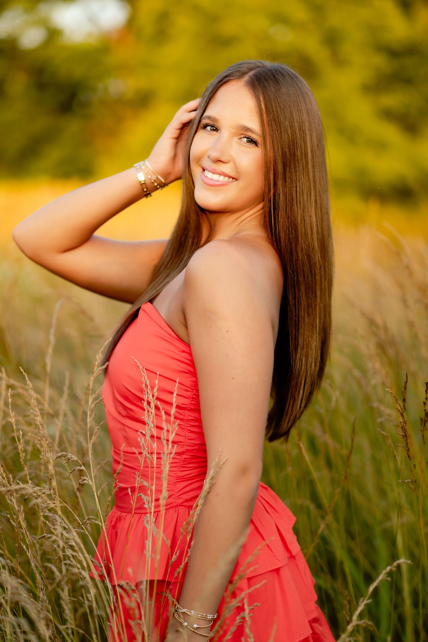 Summer portrait of someone in a coral dress posing in tall grass during golden hour.