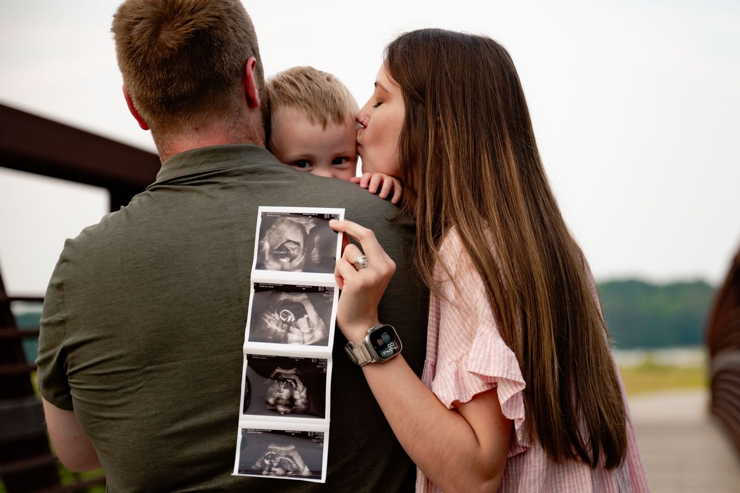 Family sharing intimate moment while holding ultrasound photos outdoors.