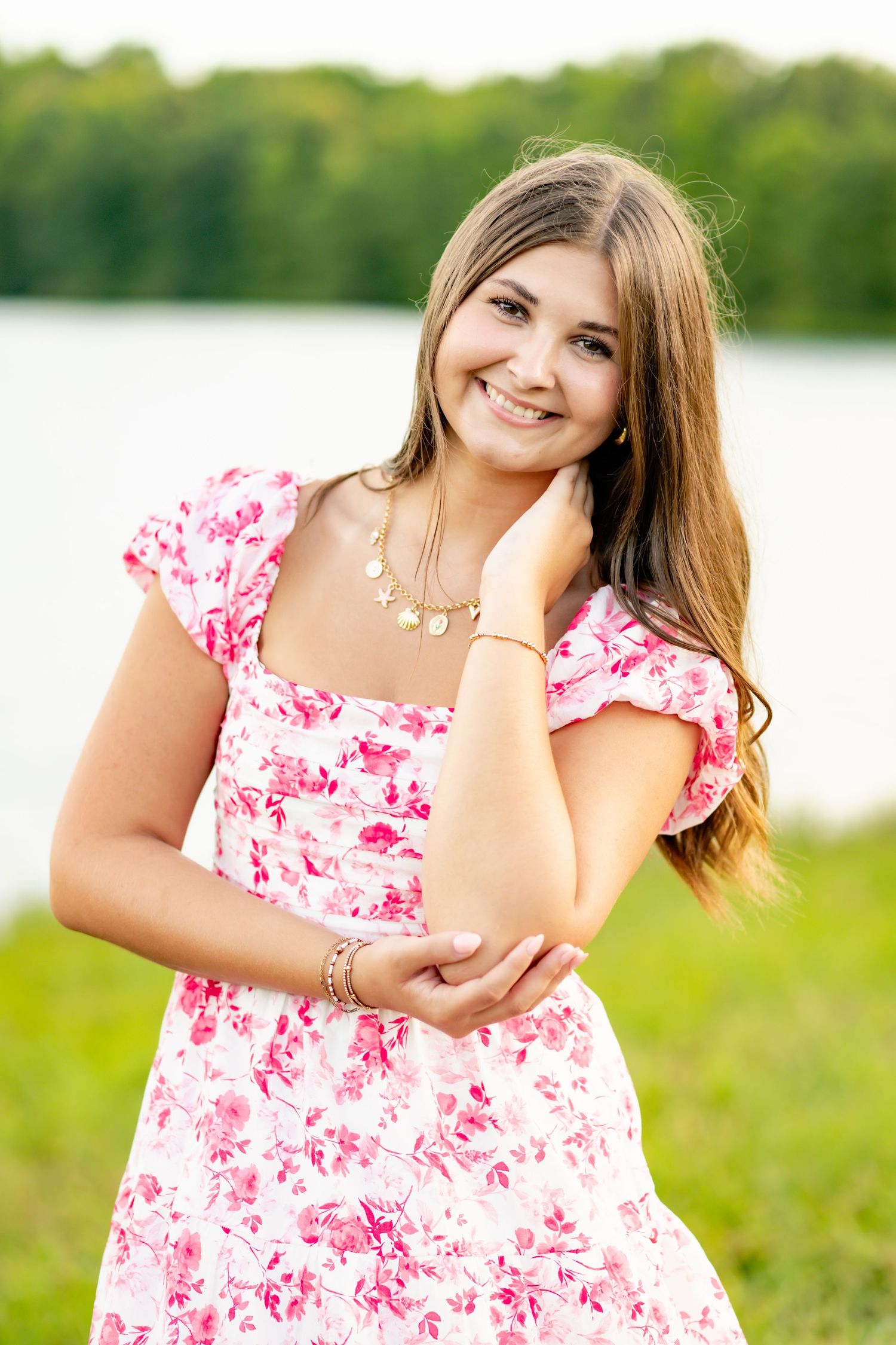 Portrait in a pink floral dress against a lakeside background with natural sunlight.