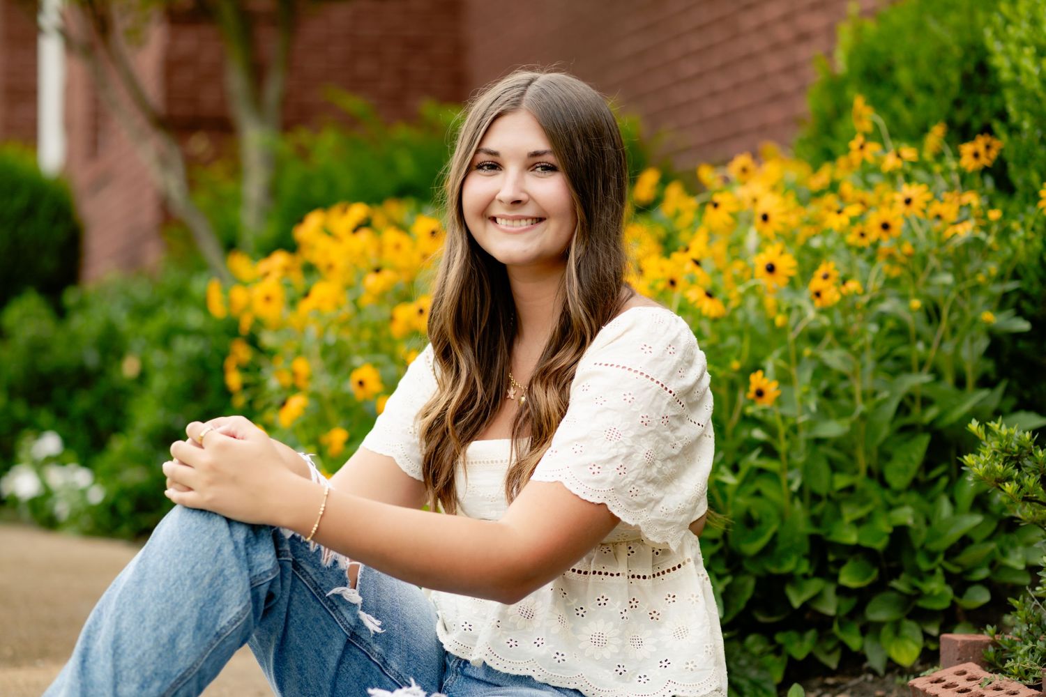 Woman in white blouse sitting outdoors among vibrant yellow rudbeckia flowers on a summer day.