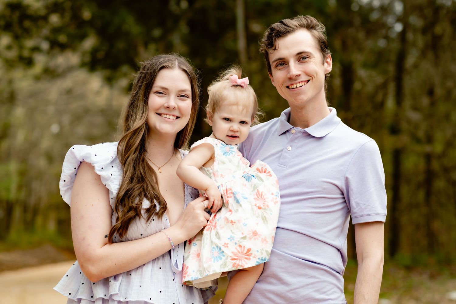 Family of three posing for outdoor portrait in spring attire.