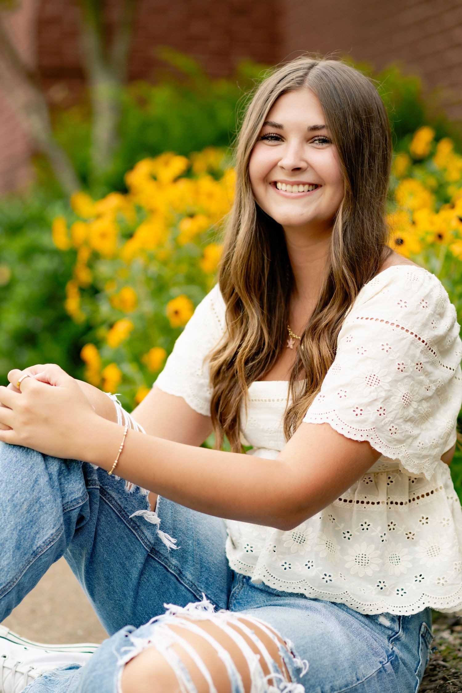 Casual outdoor portrait wearing white eyelet top and distressed jeans among yellow flowers.