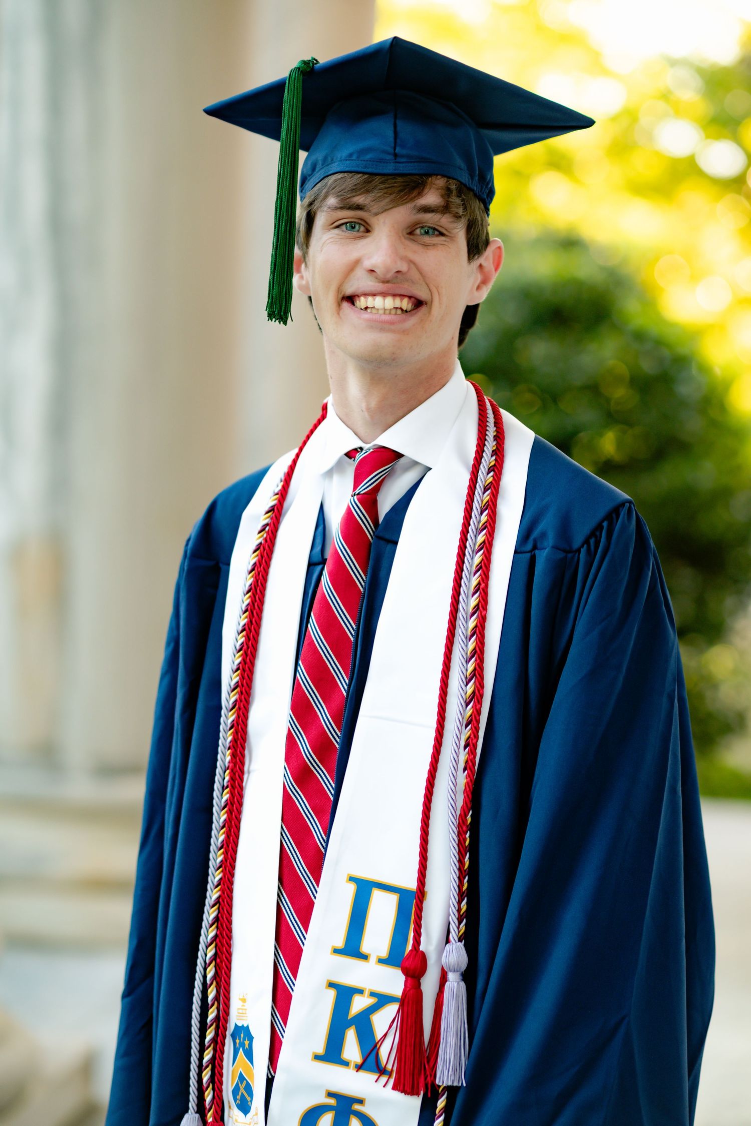 Graduate shows decorated stoles on navy graduation gown against pillared background.