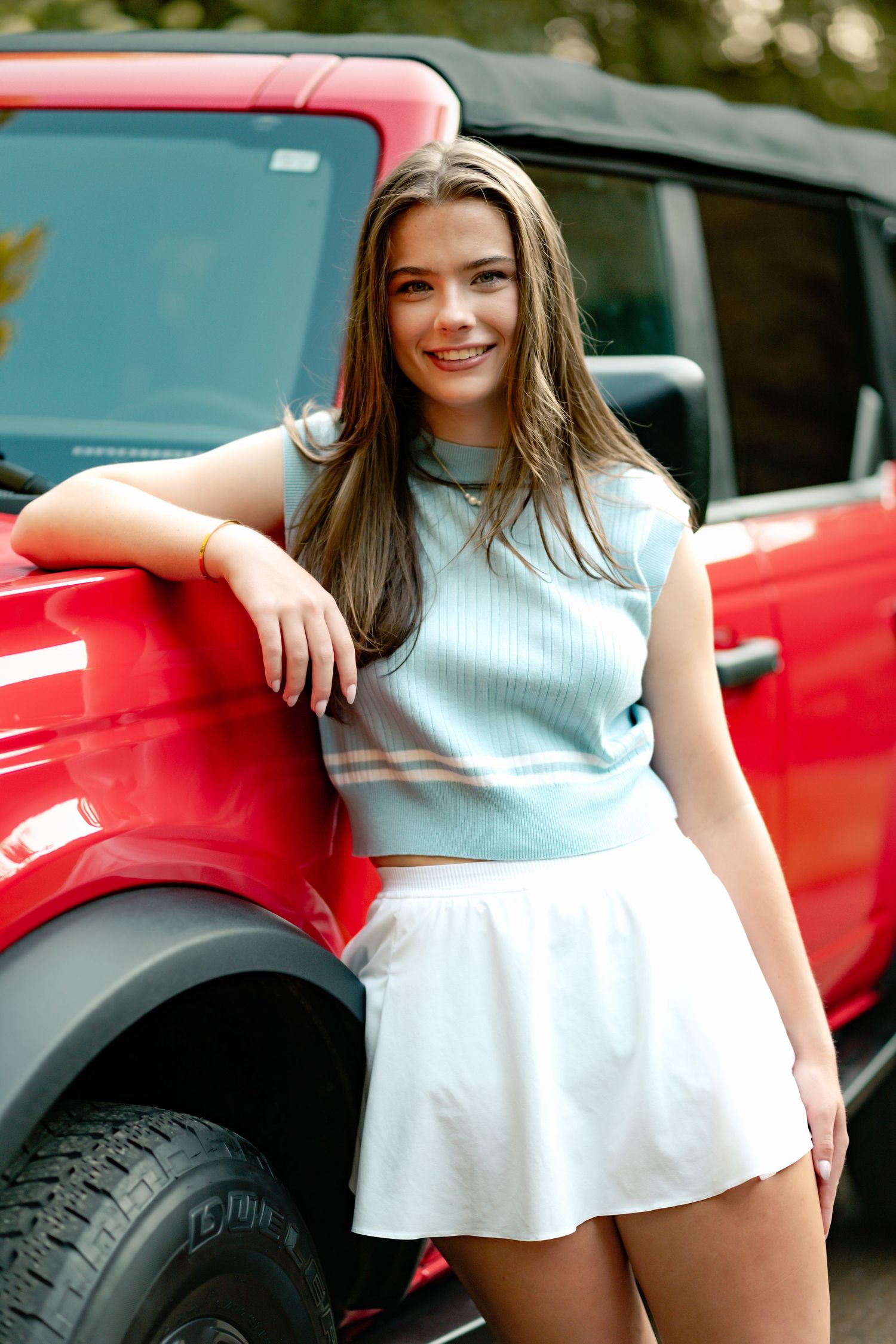 Casual summer fashion look with light blue crop top and white skirt posed next to a red SUV outdoors.