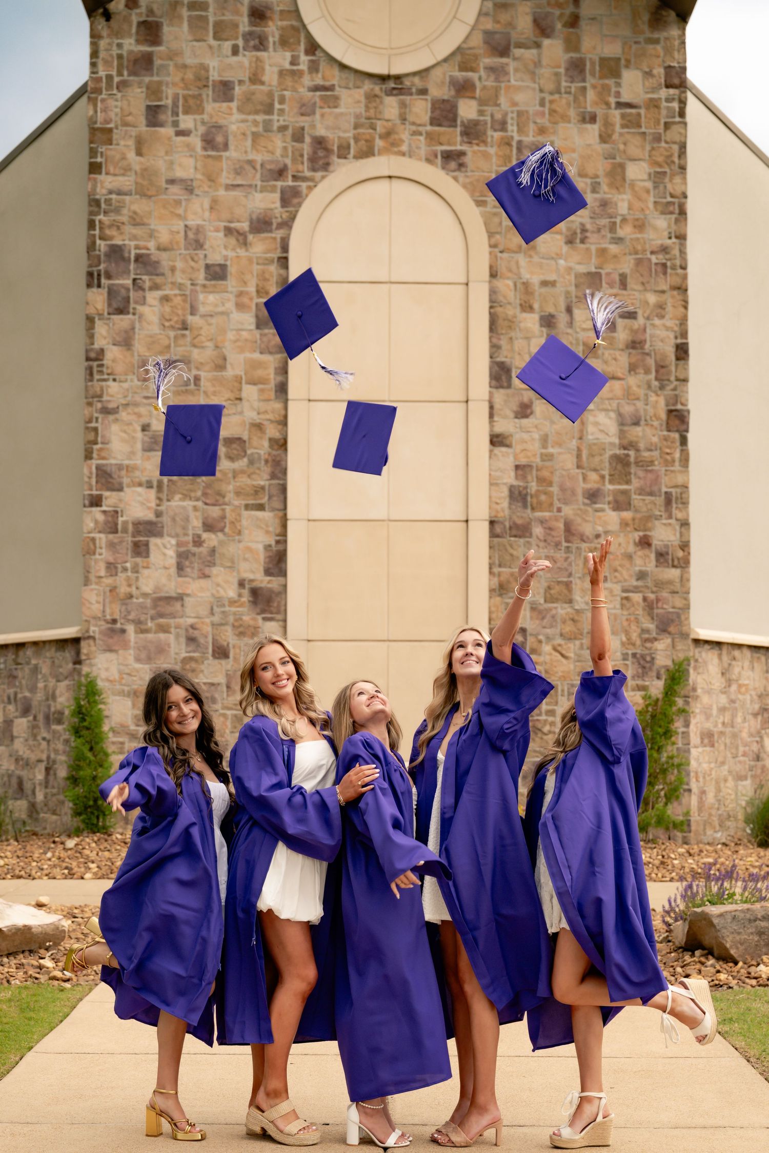 Graduates toss blue caps in the air against stone building backdrop.