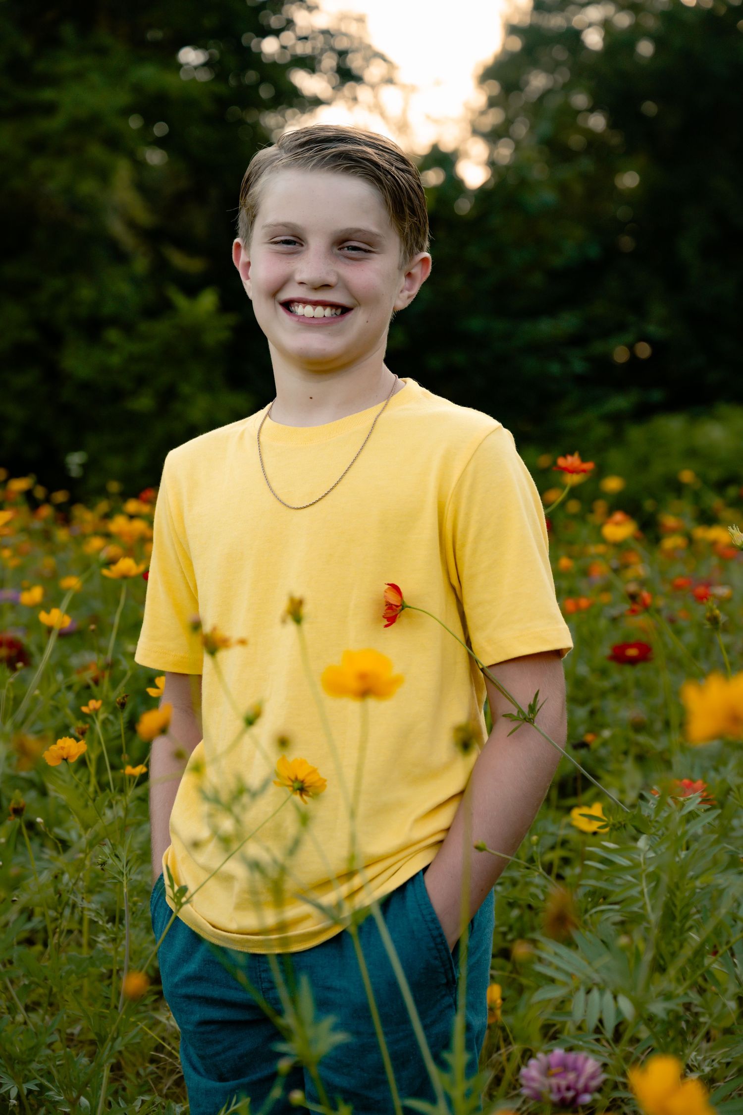 Child wearing yellow t-shirt standing among colorful wildflowers in a summer garden at sunset.