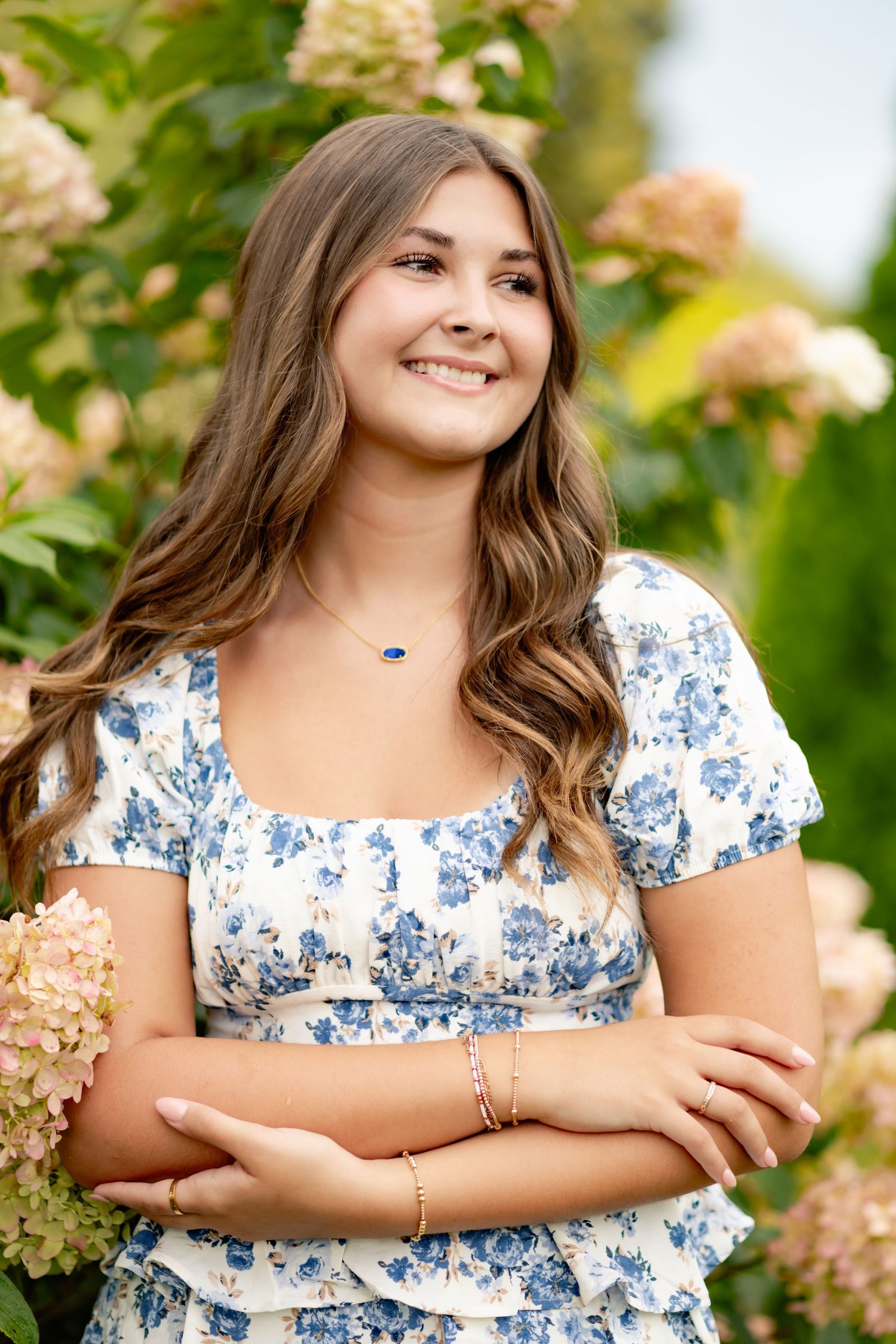 Portrait in floral dress standing among blooming hydrangea bushes in garden.