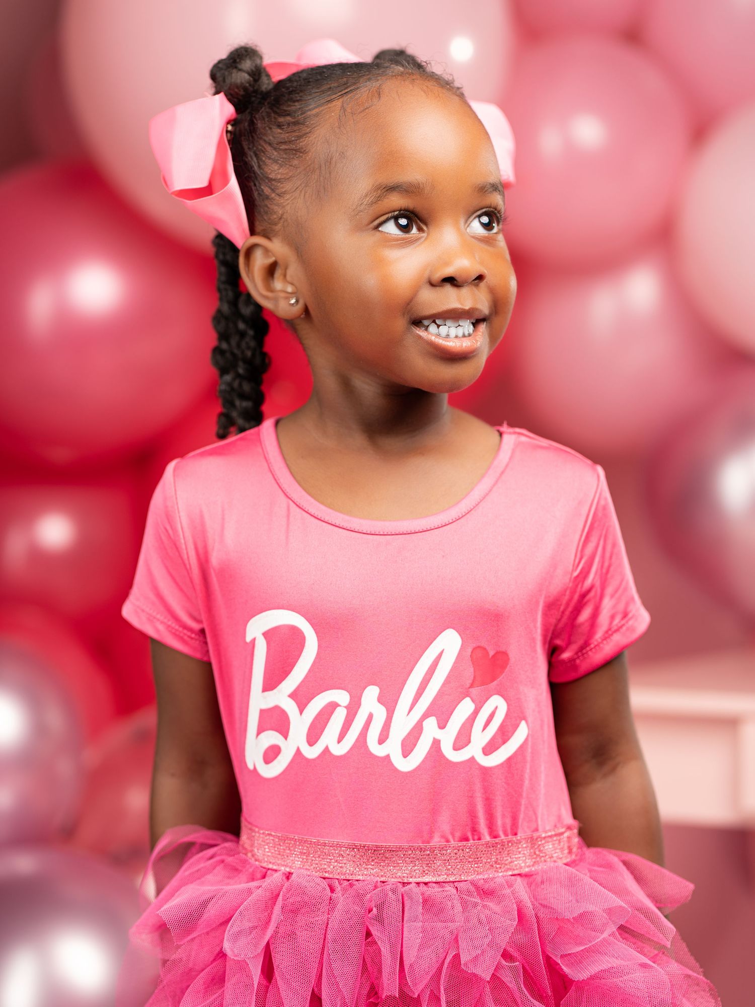 Pink party setting with Barbie-themed attire and festive balloon decorations in shades of rose and silver.