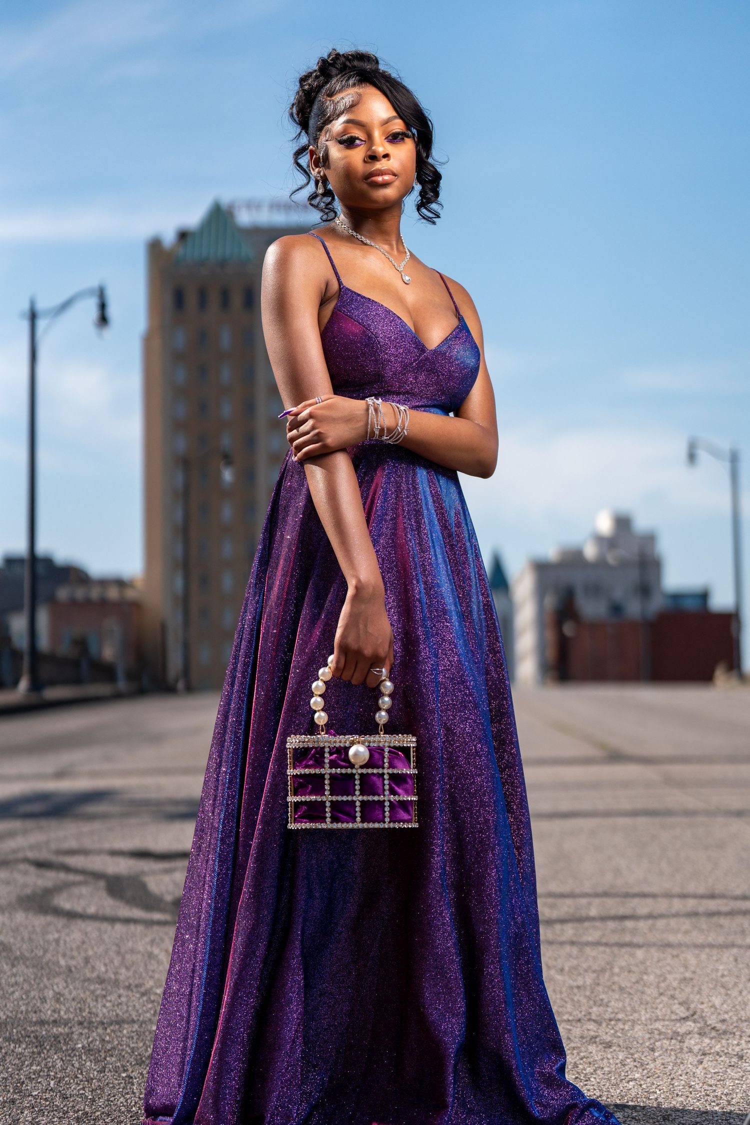 Elegant sparkly purple formal gown with matching metallic handbag photographed on urban rooftop.