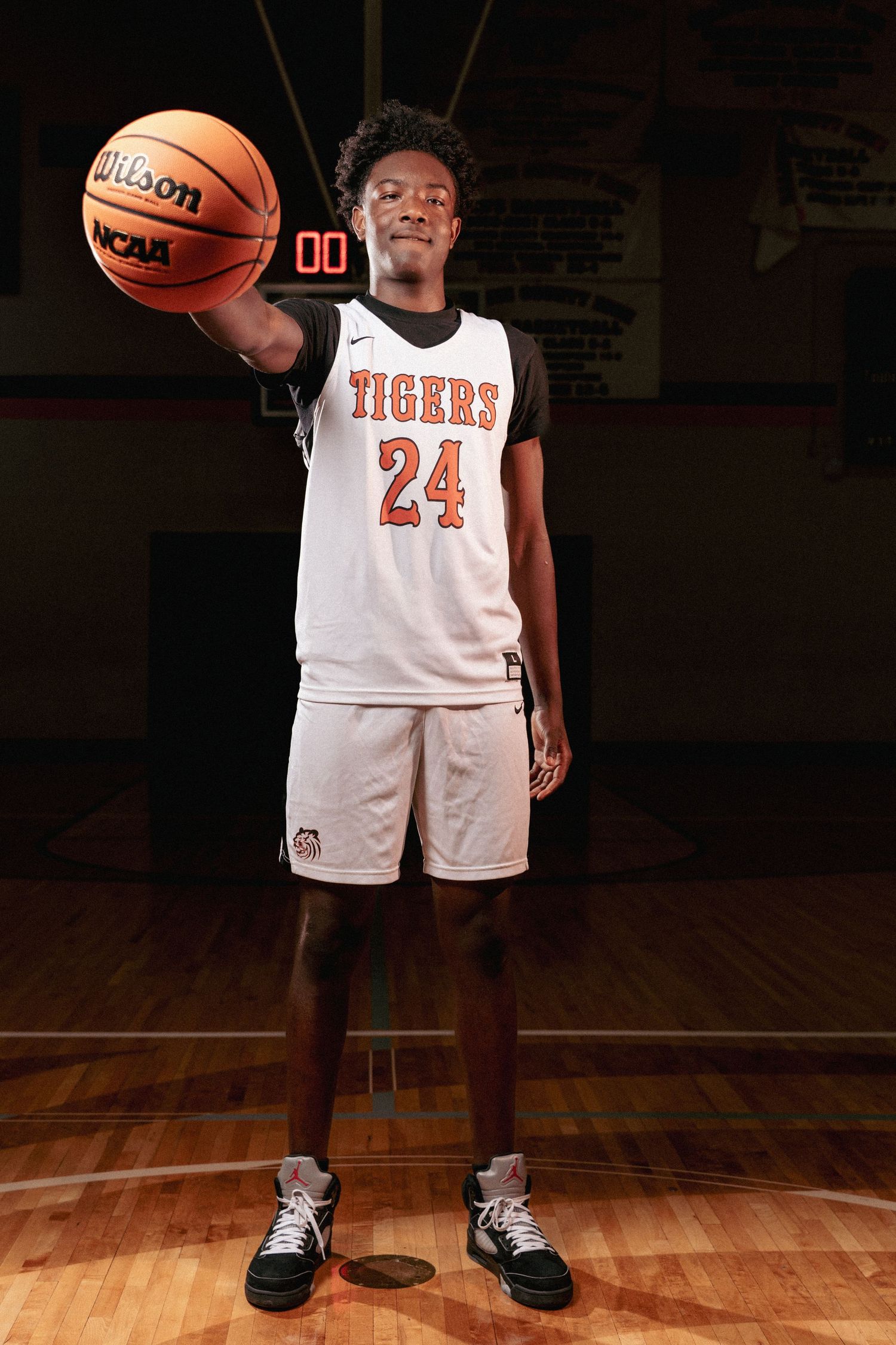 Low angle view of basketball player in white Tigers jersey standing on wooden court with Wilson basketball.