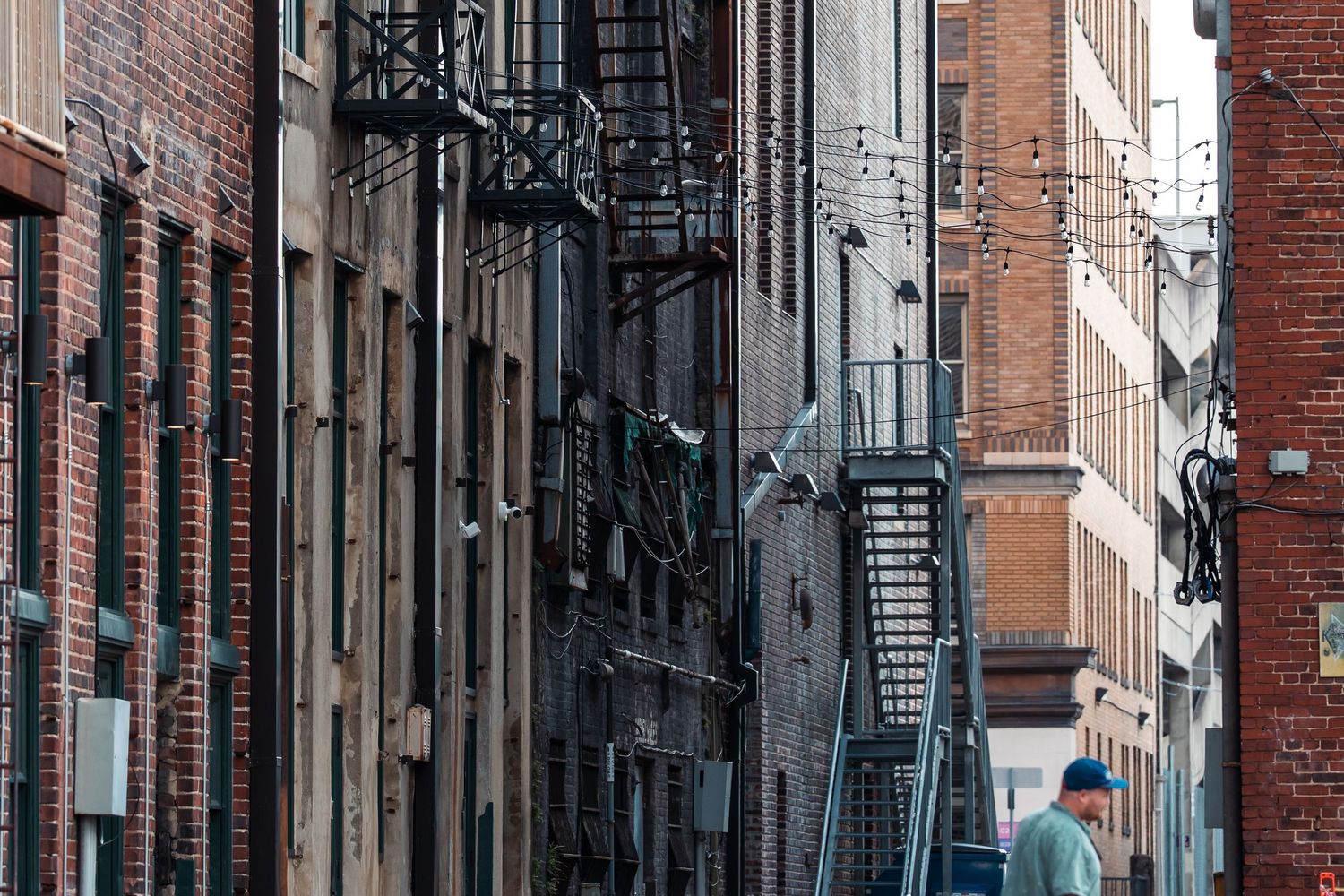 Urban alley with brick buildings and fire escapes in a narrow passageway.