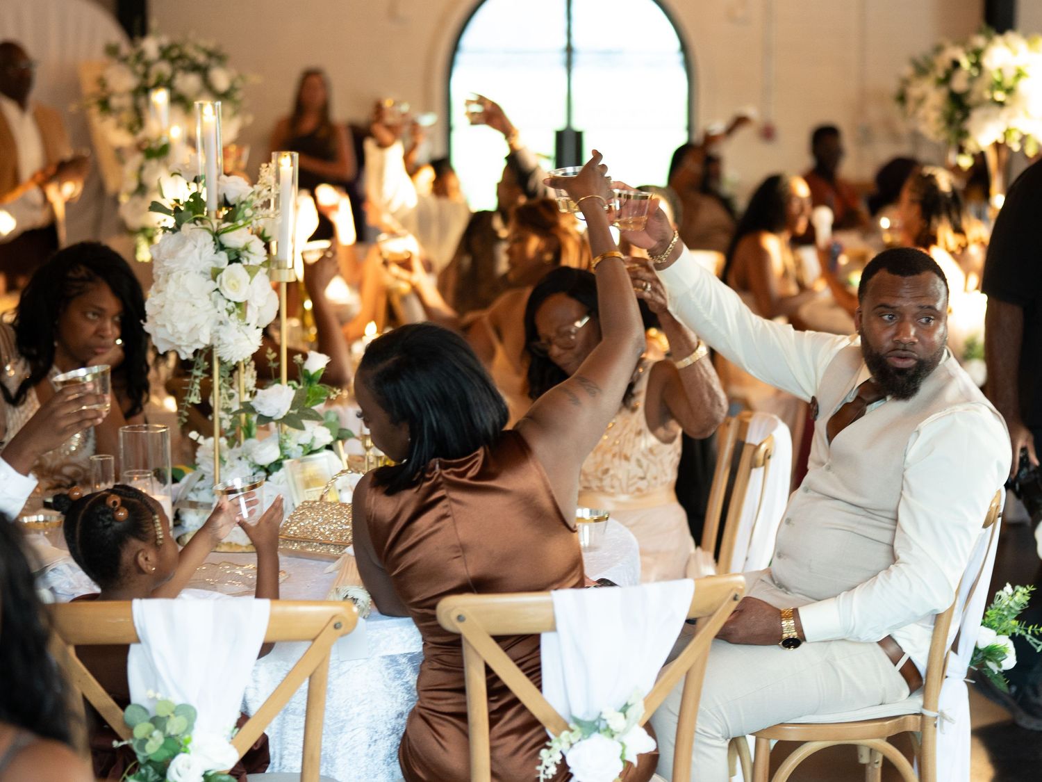 Elegant wedding reception with guests raising glasses in a toast at a beautifully decorated table with white floral arrangements.