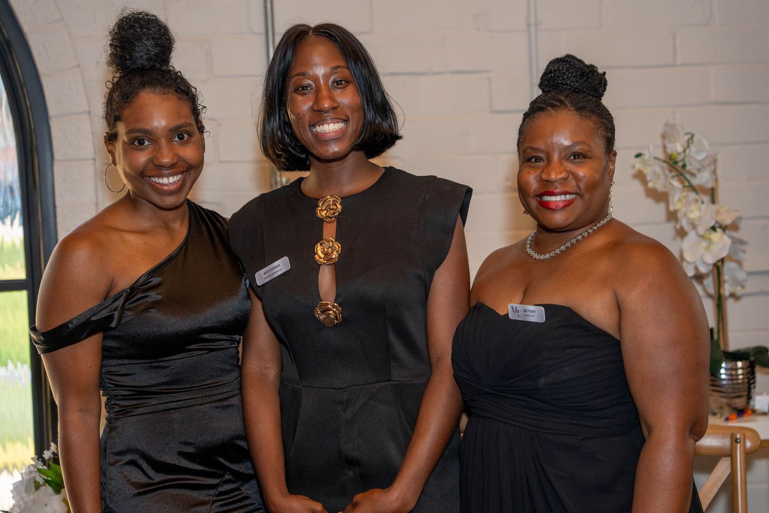 Three women in elegant black formal attire smiling together at a sophisticated evening event.