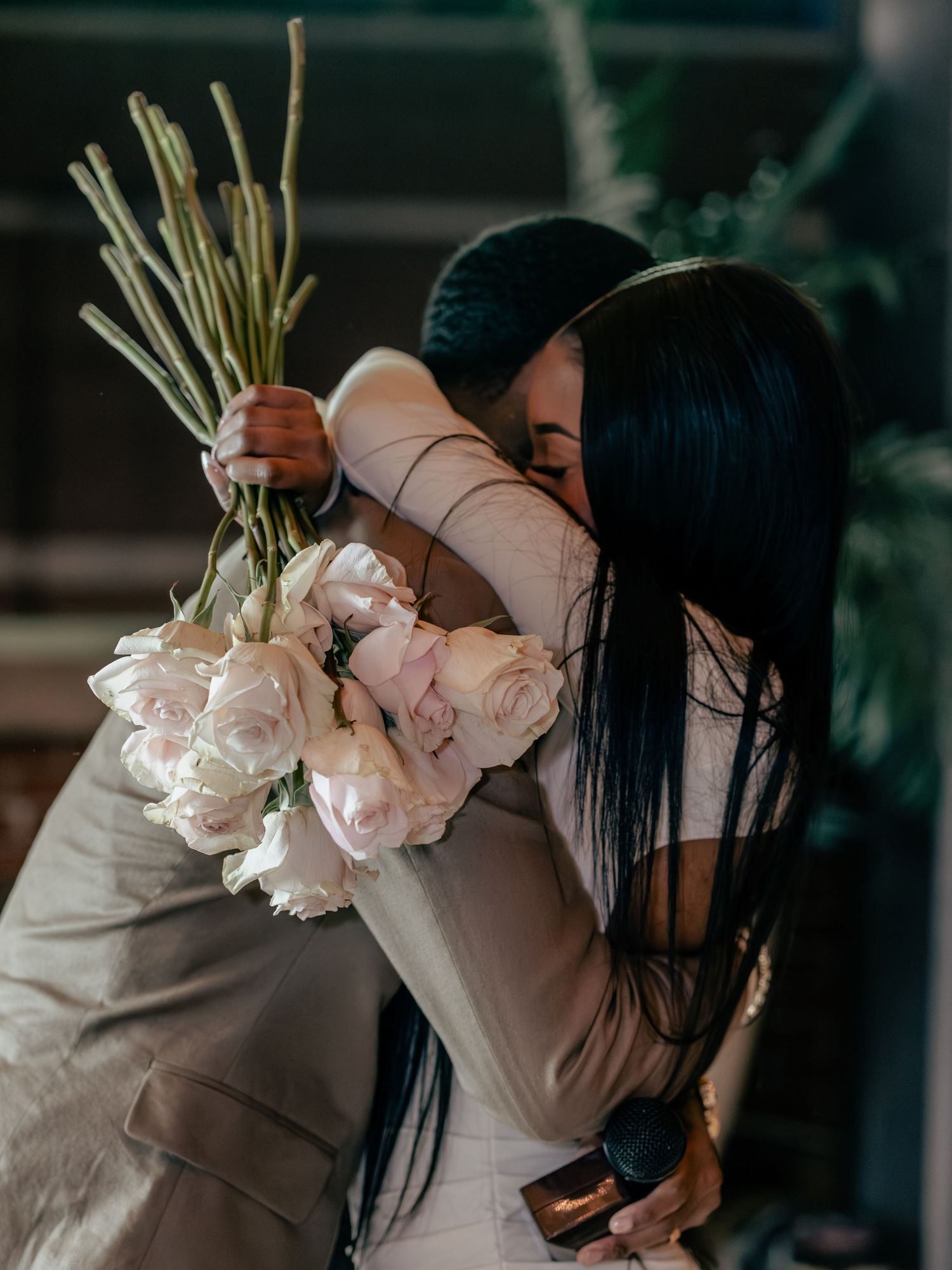 A person holds a bouquet of soft pink peonies and roses while covering their face in a moody indoor setting.