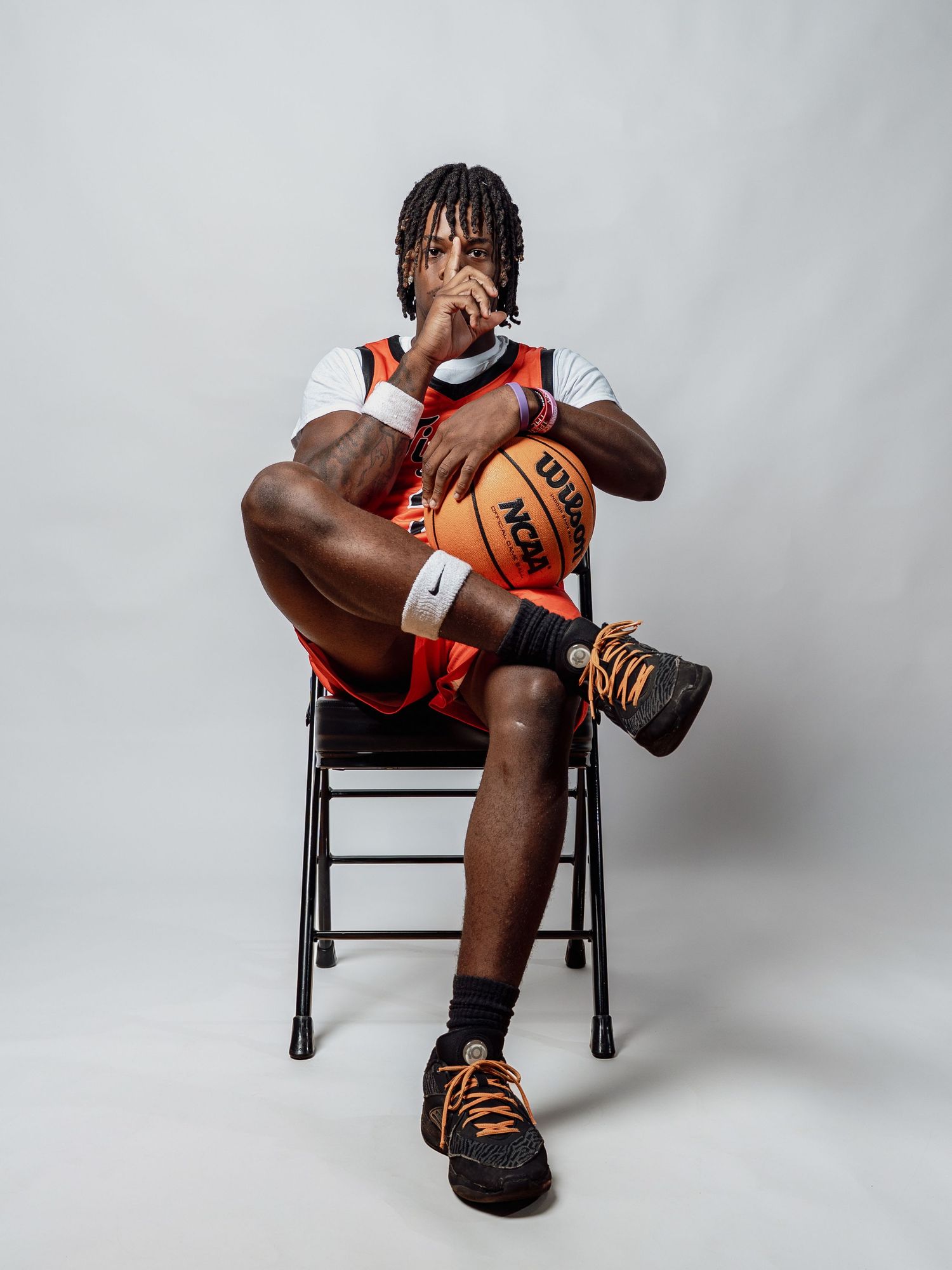 Basketball player in an orange jersey sits on a folding chair holding a Wilson NCAA basketball in a studio portrait.