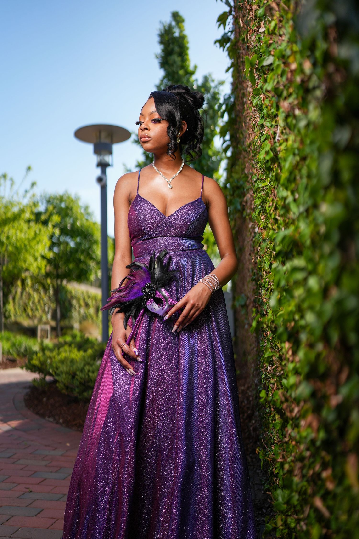 Stunning purple sparkle evening gown photographed in a garden setting with ivy backdrop.