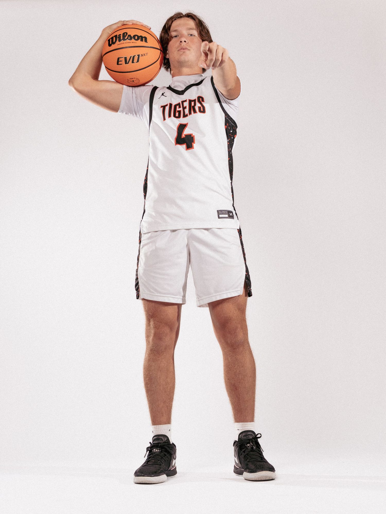 Basketball player in white Tigers uniform poses with ball against white background.