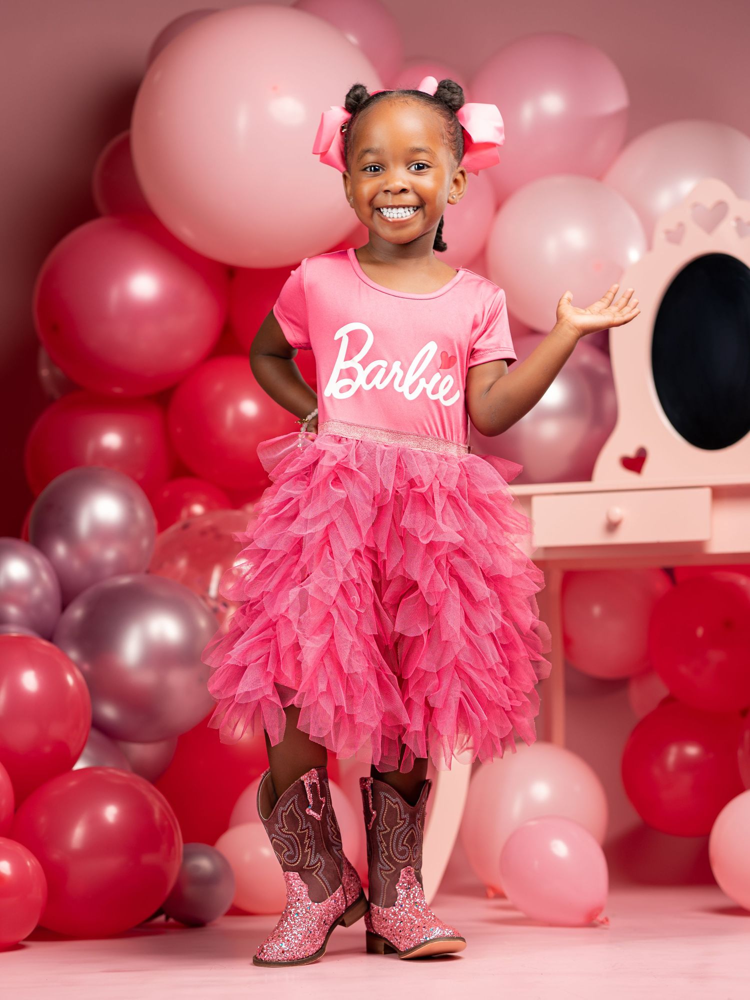 Playful pose in a pink tulle Barbie dress with sparkly shoes amidst a balloon-filled party backdrop.