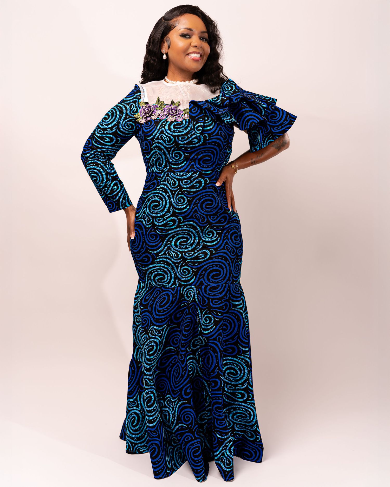 A model showcases a navy and turquoise African print dress with ruffled sleeves and a flared silhouette.