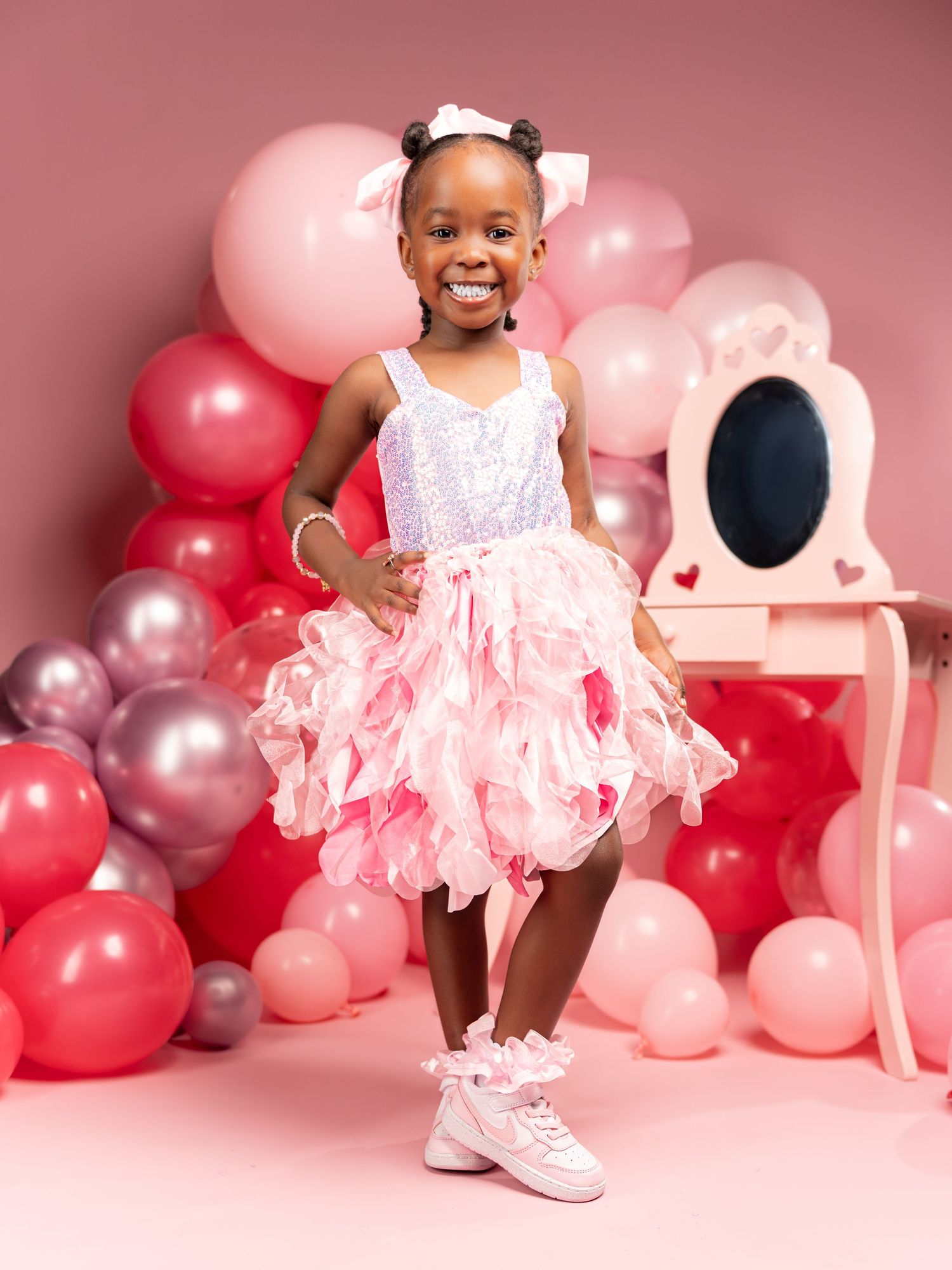 Joyful celebration scene with pink and silver balloons and white lace dress against a rosy backdrop.